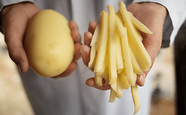 Zwei Hände, eine hält eine ganze Kartoffel, die anderen einige Pommes Frites