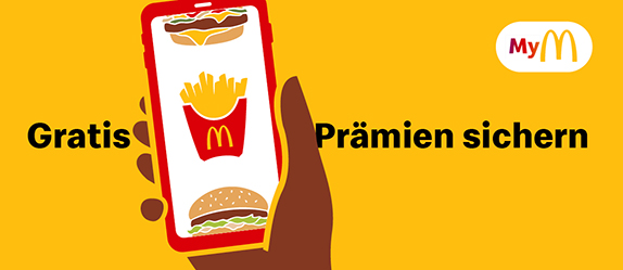 Im Vordergrund eine Hand, die ein Smartphone hält, auf dem die McDonald’s App geöffnet ist. Im Hintergrund der Hinweis zum Bonusprogramm MyMcDonald’s und der Aussage „Gratis Prämien sichern“.