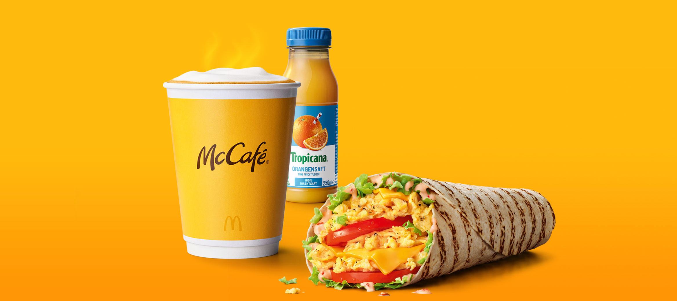 Das Bild zeigt einen dampfenden Becher Kaffee, einen McWrap® Rührei Cheese und einen Orangensaft.