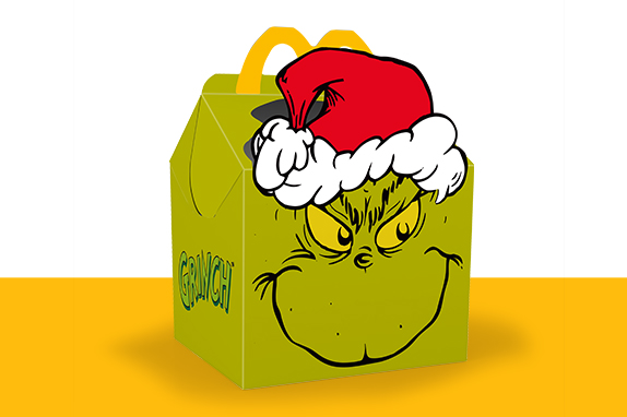 The Grinch’s™ face with a Christmas hat on the Happy Meal box on top of a yellow shelf.