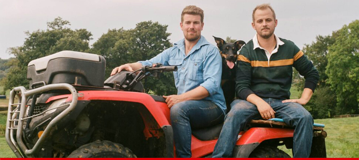 Two farmers and a dog sitting on a tractor.